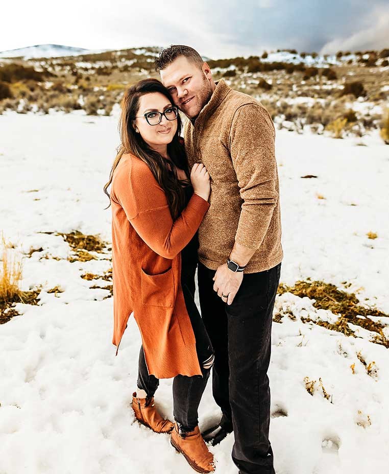 A couple posing for a photo by a snowy hillside